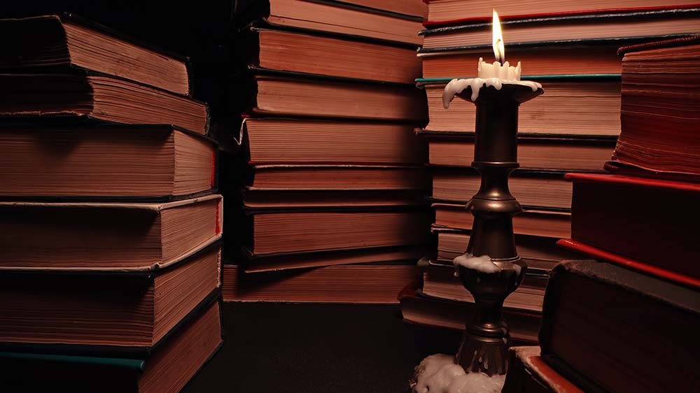 Livros em uma mesa de biblioteca iluminados por uma vela.